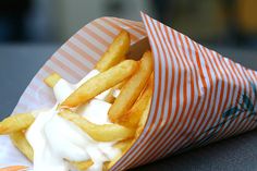 a close up of french fries in a wrapper with sour cream on top, sitting on a table