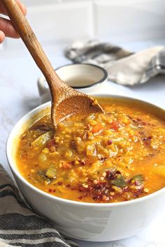 a person holding a wooden spoon over a bowl of soup