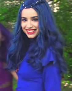 a woman with blue hair is smiling and wearing a purple dress in front of some trees