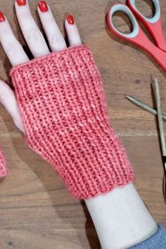 a pair of pink knitted gloves sitting on top of a wooden table next to scissors