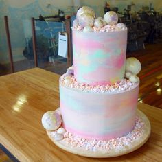 a three tiered cake with pink and blue frosting on top is sitting on a wooden table