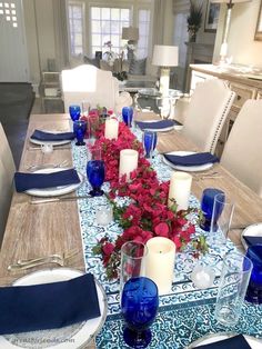 a dining room table set with blue and white place settings, candles, and flowers