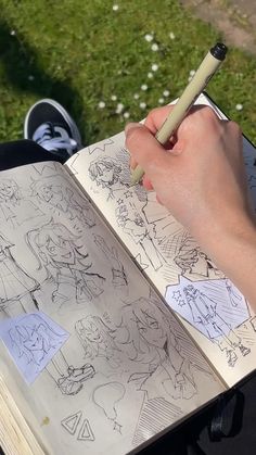 a person holding a pencil in their hand over an open book with drawings on it