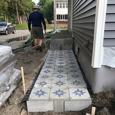 a man standing next to a house under construction with cement blocks and blue tiles on the ground