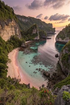 the beach is surrounded by rocky cliffs and clear blue water, with pink sand in the foreground