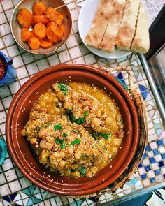 a bowl filled with food sitting on top of a table next to bowls of vegetables and bread