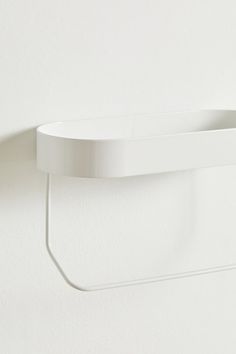 a white wall mounted shelf next to a toilet paper dispenser on the wall