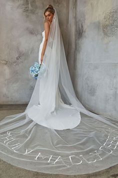 a woman in a white wedding dress with a veil on her head and flowers in her hand