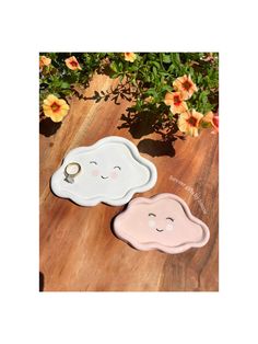 two clouds shaped dishes sitting on top of a wooden table next to flowers and plants