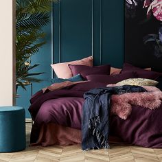 a bed with purple sheets and pillows in a room next to a blue planter