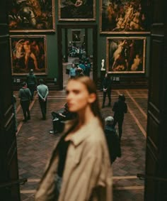 a woman walking through an art museum with paintings on the walls and people standing around