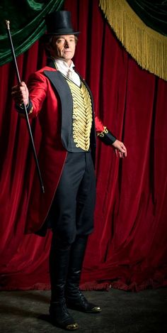 a man in a top hat and coat with a cane standing next to a red curtain