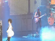 two people are on stage with guitars and one person is standing in front of them