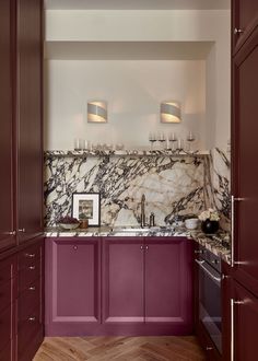 a kitchen with purple cabinets and marble counter tops, along with wine glasses on the wall