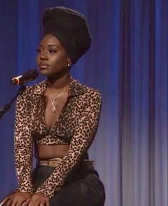 a woman sitting in front of a microphone on top of a table next to a blue curtain