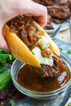 a hand is holding a sandwich with meat and cheese on it in a glass bowl