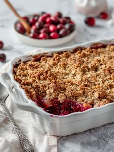 a cranberry crisp in a white dish next to a bowl of cherries