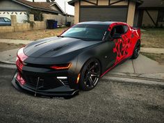 a black chevrolet camaro with red flames painted on it's hood parked in front of a house