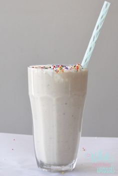 a glass filled with milk and sprinkles on top of a white table