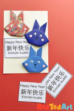 three paper animals on a red surface with happy new year written in chinese and english