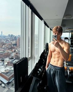 a shirtless man taking a selfie in front of a window overlooking the city