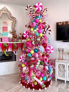 a pink christmas tree with candy and candies on it in front of a fireplace