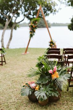 an outdoor ceremony setup with chairs and tropical flowers on the grass by the water's edge