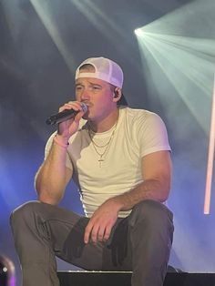 a man sitting on top of a stage while holding a microphone in his right hand