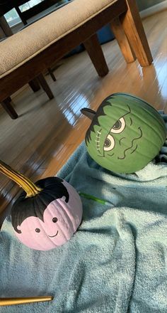 two pumpkins with faces painted on them sitting on a towel in front of a chair