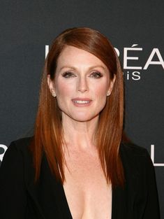 a woman with long red hair wearing a black suit and diamond earrings on her head