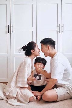 a man and woman sitting on the floor with a small boy in front of them