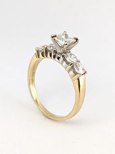 a three stone diamond ring on a white surface with the center setting in yellow gold