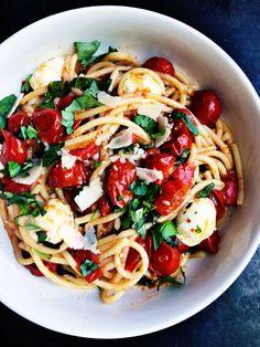 a white bowl filled with pasta covered in tomatoes and parmesan cheese, garnished with fresh herbs