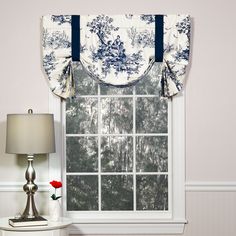 a window with a blue and white flowered valance next to a lamp on a table