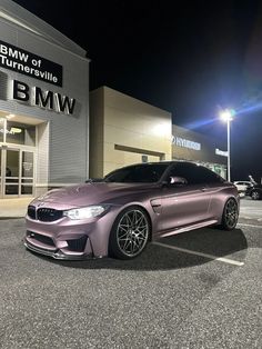 a purple car parked in front of a bmw dealership at night with the lights on