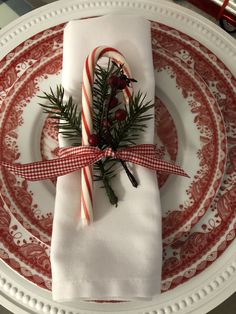 a christmas place setting with candy canes and greenery wrapped in red ribbon on a white plate