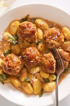 a white plate topped with meatballs covered in gravy next to a glass of wine