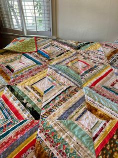 a quilted bed with many different colors and patterns on the bedspread, next to a window