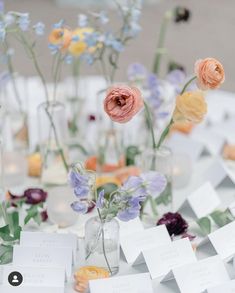 there are many flowers in glass vases on the table with name cards attached to them