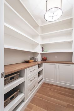 an empty kitchen with white cabinets and wood flooring on one side, open shelves in the other