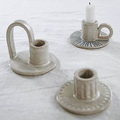 two tea cups and a candle holder on a white table cloth with a silver saucer