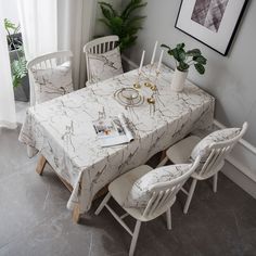 a dining room table with white chairs and a marble patterned table cloth on top of it