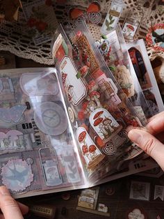 a person is holding an open book with stickers on it and some doily in the background