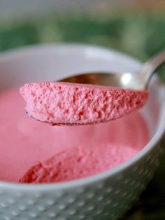 a spoon full of pink colored powder in a white bowl