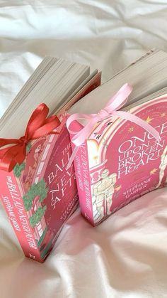 two pink books with bows on them sitting on a bed