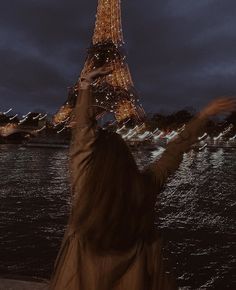 a woman standing in front of the eiffel tower with her arms raised up