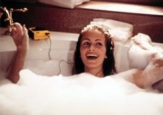 a woman is laughing in the bathtub with foam