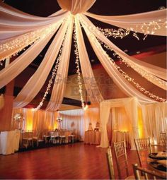 the inside of a banquet hall decorated with white drapes and lights