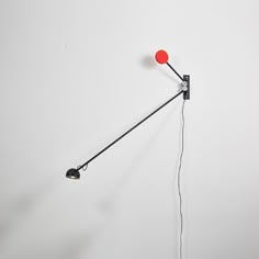 a red light hanging from the side of a wall next to a black lamp on a white wall