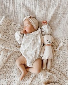 a baby laying on top of a bed next to a teddy bear